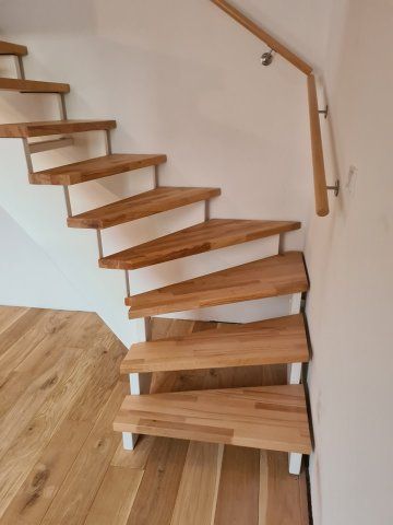 Schwebende Holztreppe mit Metallstützen und einem Holzhandlauf vor einer weißen Wand.