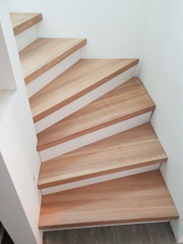 Holztreppe mit weißen Zierleisten vor einer weißen Wand.