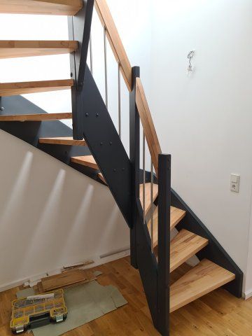 Moderne Holztreppe mit schwarzen Metallstützen und einem Holzhandlauf.