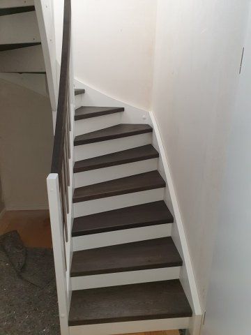 Treppe mit dunklen Holzstufen, weißen Setzstufen und Geländer vor weißen Wänden.