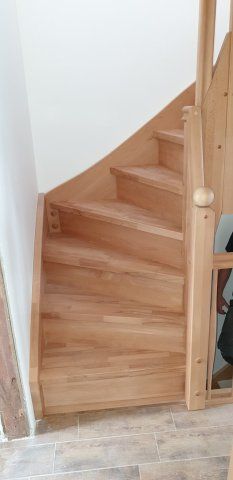 Holztreppe mit geschwungenen Stufen, helle Holzfarbe, weiße Wand.