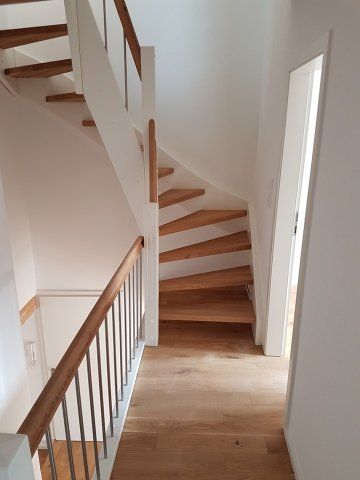 Holztreppe mit weißen Wänden und holzfarbenem Bodenbelag. Handläufe auf beiden Seiten.