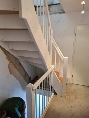 Weiß gestrichene Treppe mit Geländer; Person, die in der Nähe einer beschädigten Wand arbeitet.