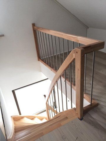 Holztreppe mit Metallgeländer, hellem Holz und hellem Treppenabsatz.