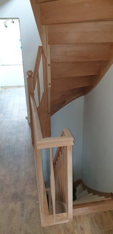 Holztreppe mit Geländer, von oben gesehen. Helles Holz, weiße Wände und gefliester Boden.