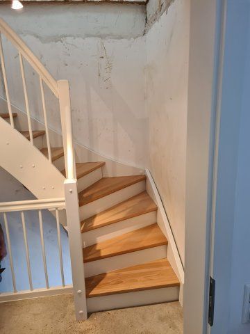 Holztreppe mit weißem Geländer, die in einem weißen und hellen Innenraum nach oben führt.