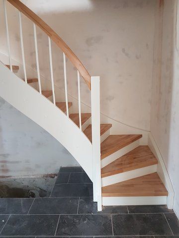 Treppe mit weißem Geländer, Holzstufen und Handlauf vor einer Gipswand; dunkler Fliesenboden.