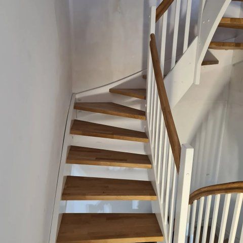 Hölzerne Wendeltreppe mit weißem Geländer vor einer weißen Wand.