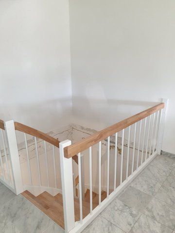 Treppe mit weißen Balustern, hellem Holzhandlauf und Holzstufen.