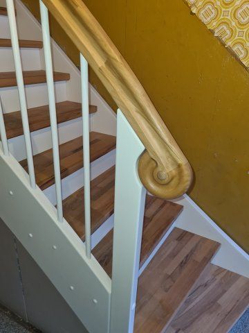Holztreppe mit weißem Geländer, Holzhandlauf und gelber Wand.