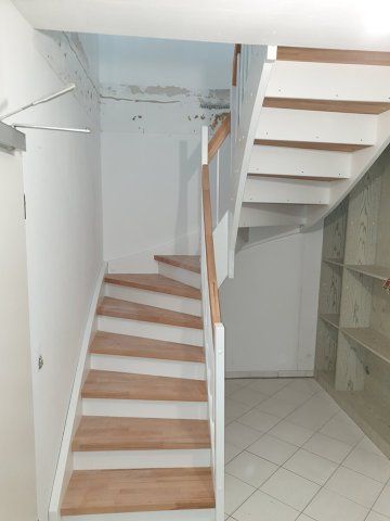 Treppe mit Holzstufen und weißen Setzstufen, einem Holzhandlauf und weißen Wänden.