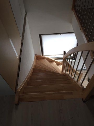 Hölzerne Wendeltreppe mit Metallgeländer, die nach oben zu einem Fenster führt.
