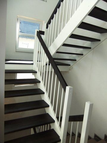 Treppe mit weißem Geländer, dunklen Stufen und einem kleinen Fenster.