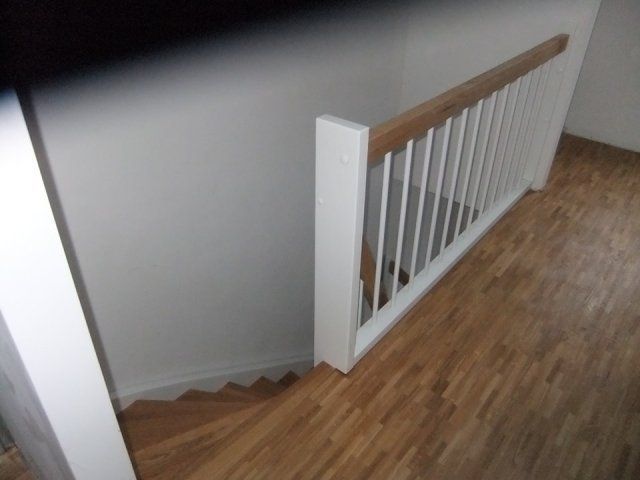 Treppe mit weißem Geländer und Holzstufen, die in einen Flur hinabführt.