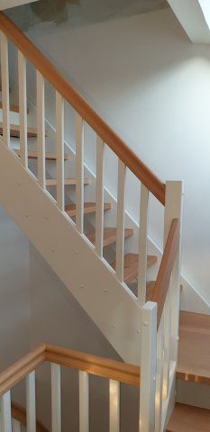 Holztreppe mit weißem Geländer, braunem Handlauf und Holzstufen.