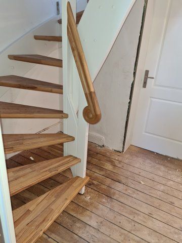 Holztreppe mit gebogenem Handlauf, neben weißer Wand und Holzboden.