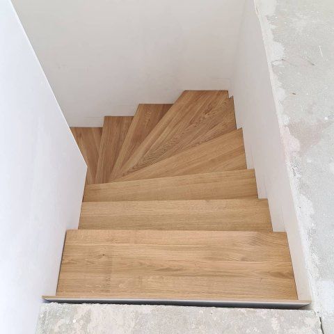 Abwärts führende Holztreppe zwischen weißen, unfertigen Wänden.