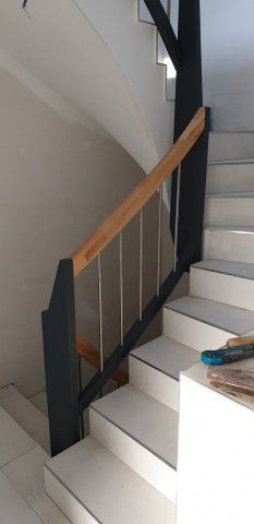 Treppe mit weißen Stufen, einem Holzhandlauf und schwarzen Metallstützen.