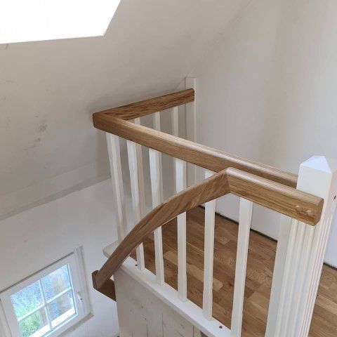 Treppe mit weißen Balustern und Holzhandläufen, von oben gesehen.