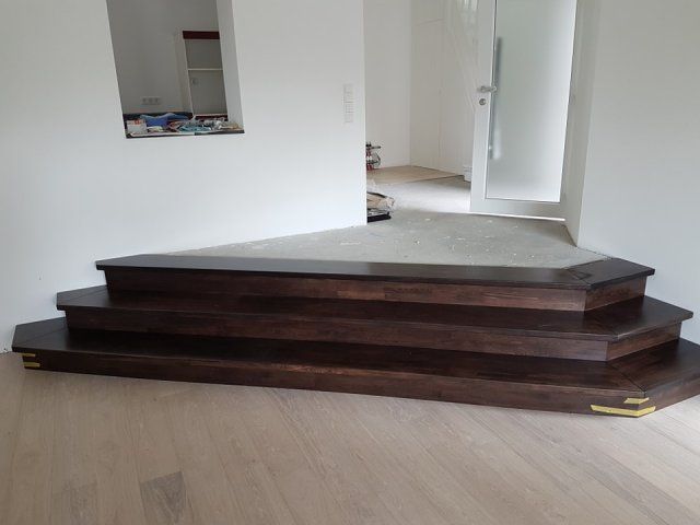 Dunkle Holzstufen führen zu einer Tür hinauf, darunter liegt ein heller Holzboden.