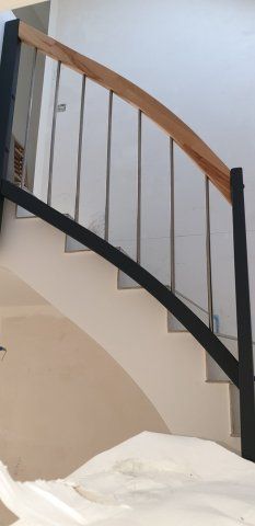 Eine Treppe mit einem geschwungenen schwarzen Geländer, Pfosten aus Edelstahl und einem Handlauf aus Holz.