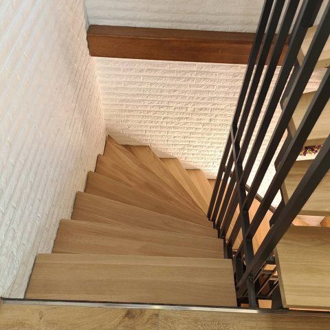 Holztreppe mit schwarzem Metallgeländer, weiße Ziegelwand.