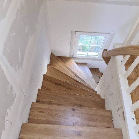 Holztreppe mit Fenster, weißen Wänden und einem Holzhandlauf.