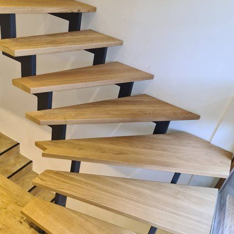 Holztreppe mit dreieckigen Stufen, getragen von schwarzen Metallklammern, vor einer weißen Wand.