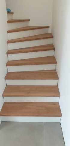 Holztreppe mit weißen Setzstufen vor weißen Wänden.