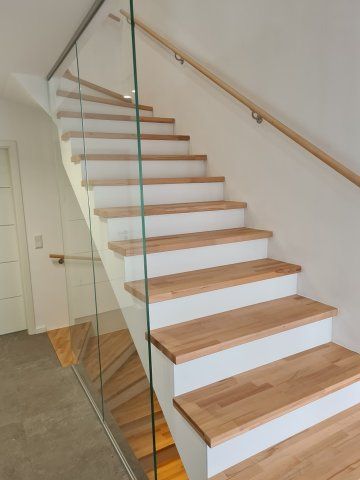 Holztreppe mit weißen Setzstufen und Glasgeländer, aus einem niedrigen Winkel betrachtet.
