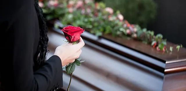 Una mujer sostiene una rosa roja delante de un ataúd.