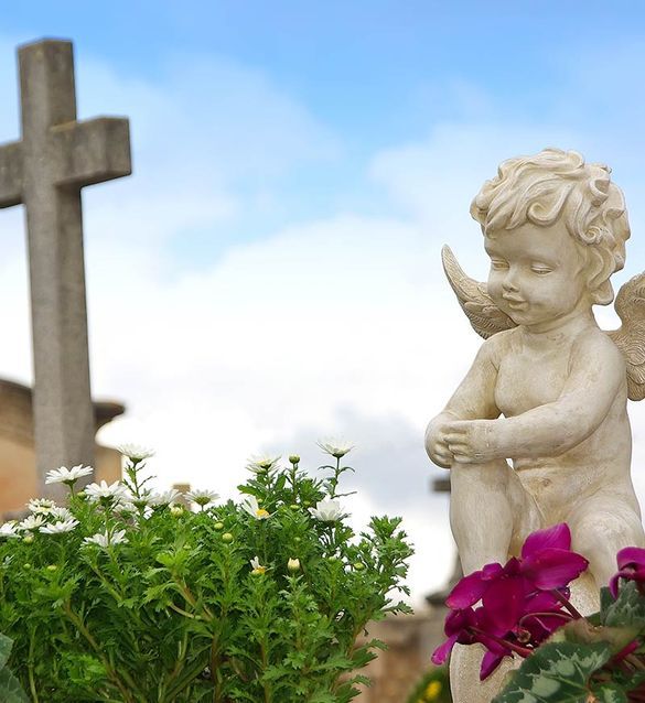 Una estatua de un querubín con una cruz al fondo.