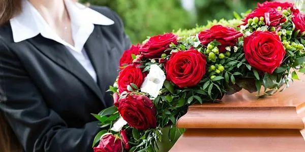 Una mujer sostiene una corona de rosas rojas delante de un ataúd.