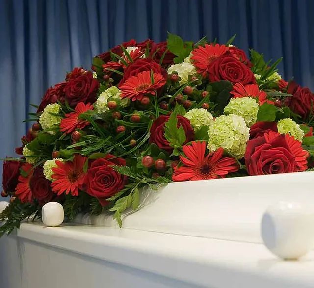 Un ataúd blanco cubierto de flores rojas y verdes.