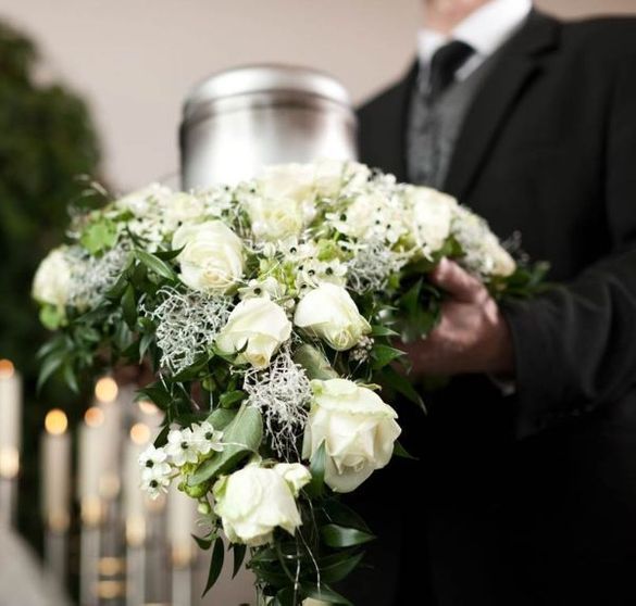 Un hombre con traje y corbata sostiene un ramo de flores blancas.