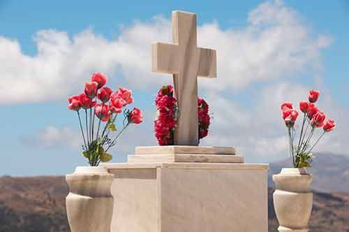 Una tumba con una cruz y jarrones con flores rojas.