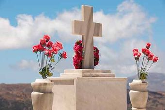 Una tumba con una cruz y jarrones con flores rojas.