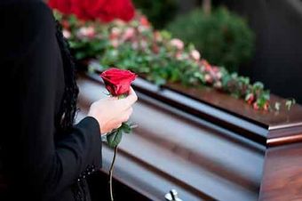 Una mujer sostiene una rosa roja delante de un ataúd.