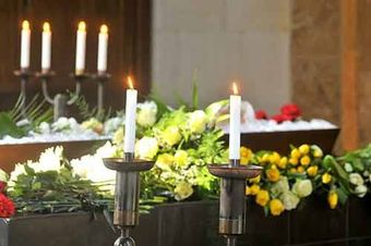 Se encienden dos velas delante de un ataúd con flores.