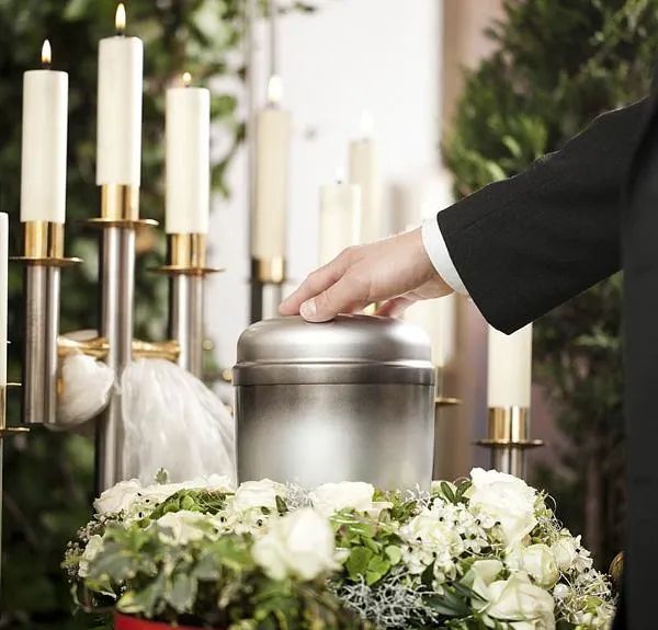 Un hombre con traje está colocando algo en una urna de metal en un funeral.