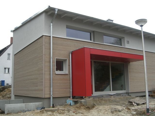 Modernes Haus mit rotem Eingang, hellbrauner Fassade und hellgrauem Obergeschoss.