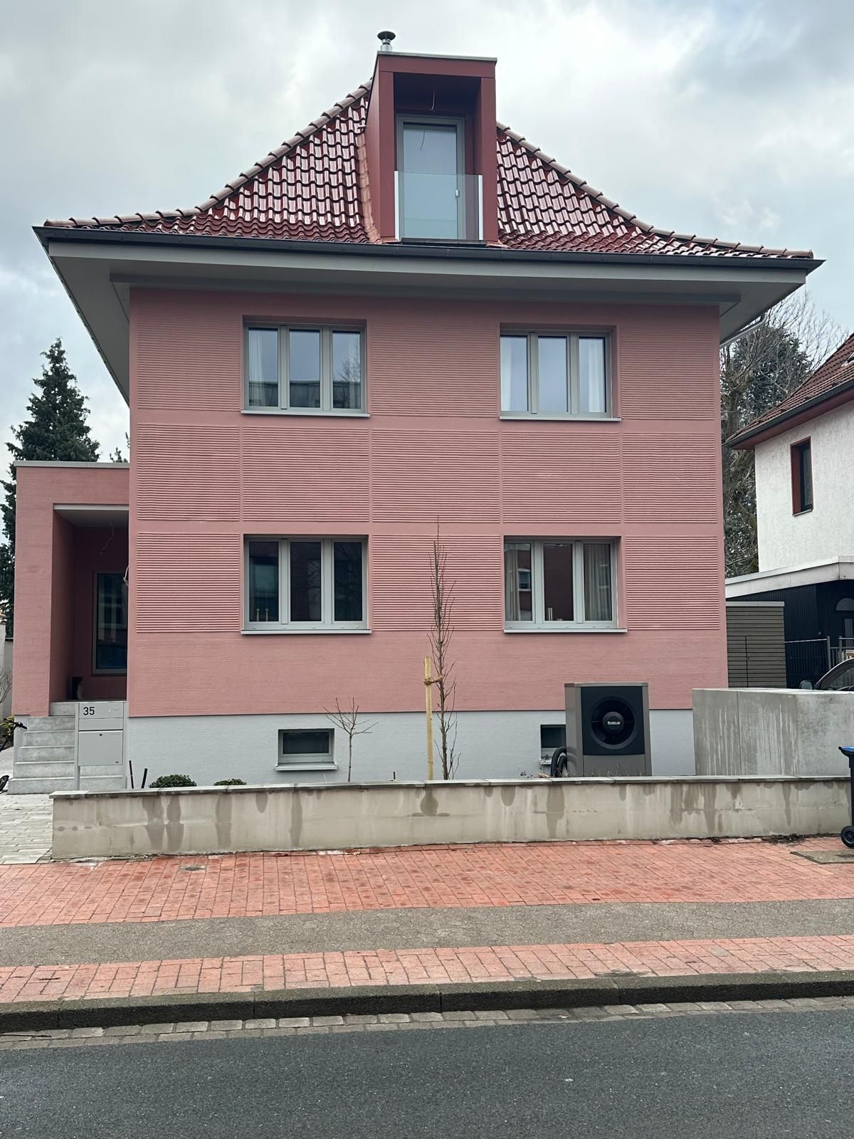 Rosafarbenes zweistöckiges Haus mit rotem Ziegeldach, kleiner Glastür und Blick auf die Straße.