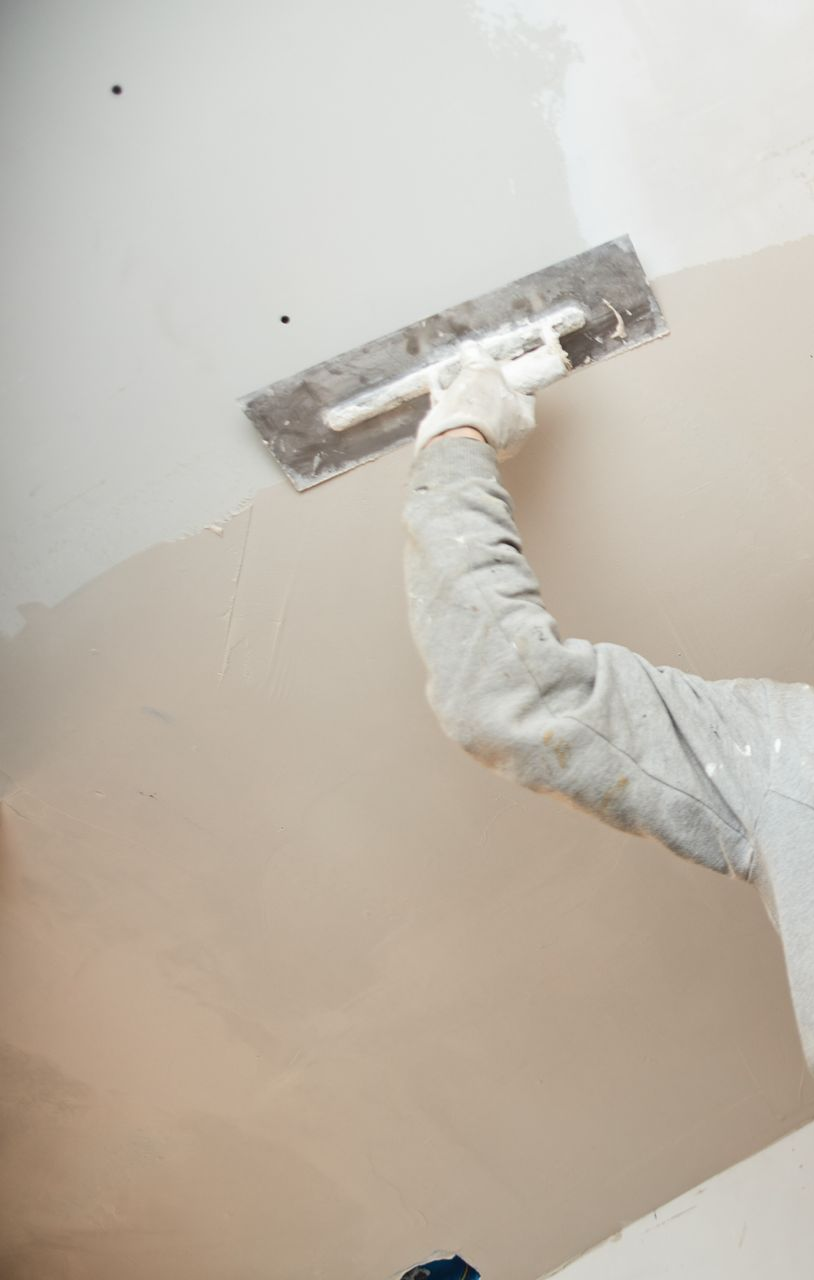 Eine Person, die mit einer Kelle Gips an eine Wand aufträgt.