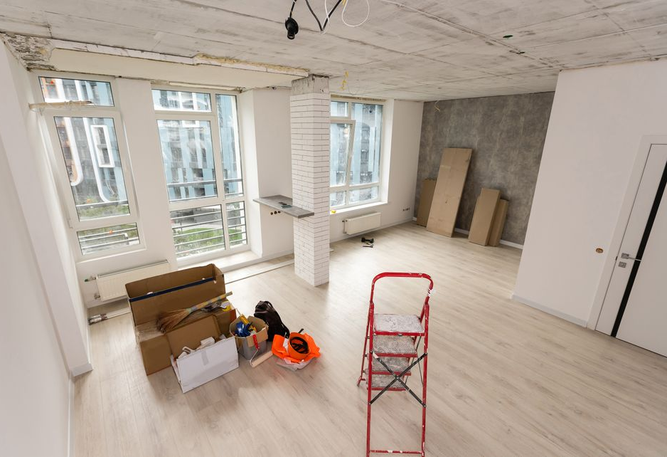 Ein Zimmer, das gerade renoviert wird, mit Pappkartons, einer Leiter und einer freiliegenden Betondecke.