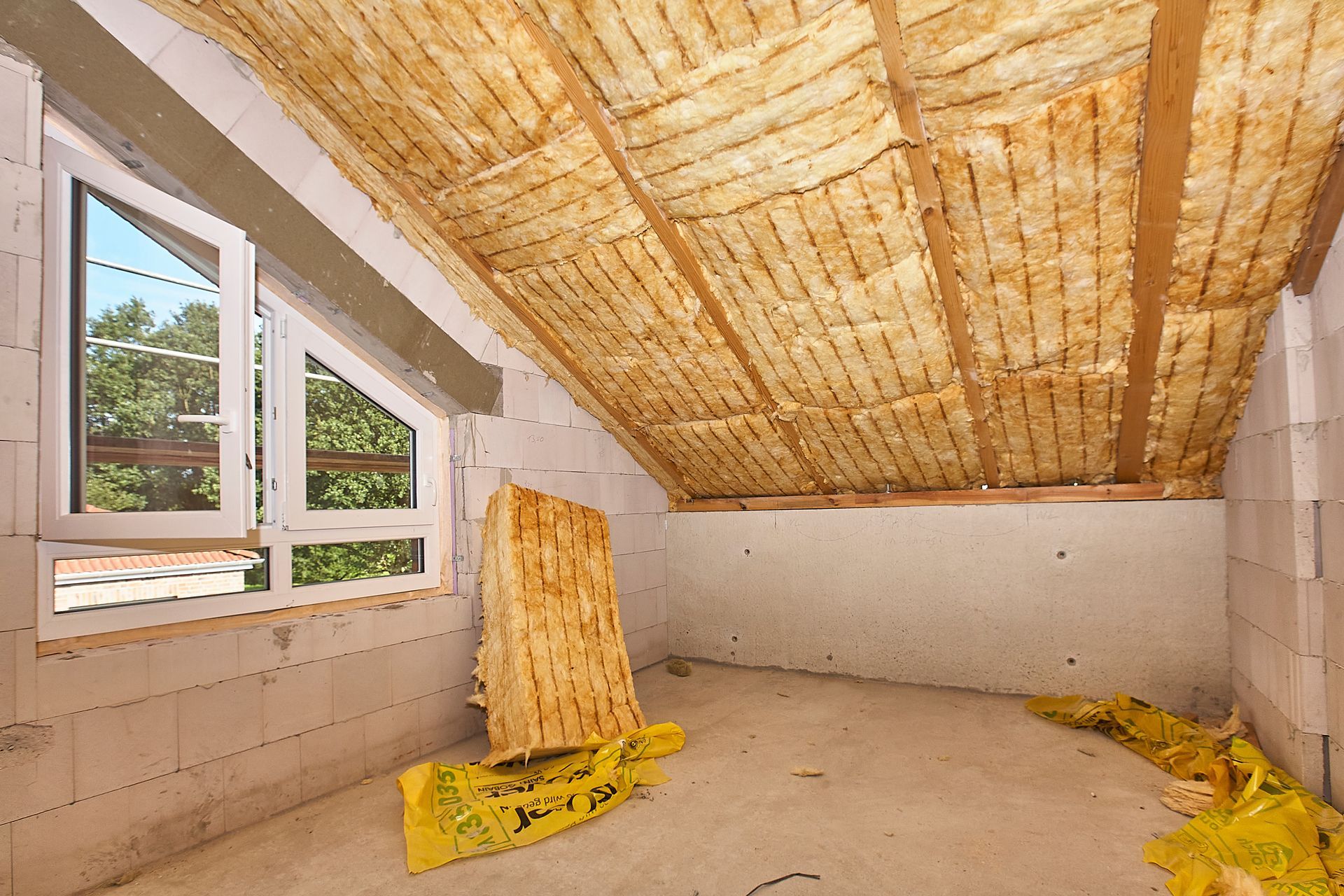 Innenansicht des im Bau befindlichen Dachbodens mit freiliegenden Holzbalken, Dämmung und Fenster.