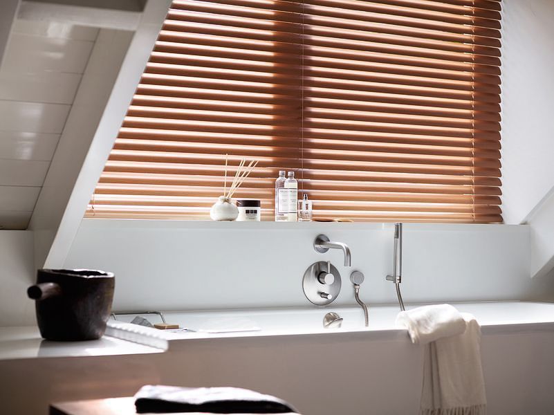 ein Badezimmer mit einer Badewanne und einem Fenster mit Holzjalousien - Sonnenschutz von Koke Raumausstattung - Tobias Liebrand - vor Ort in Senden und Lüdinghausen