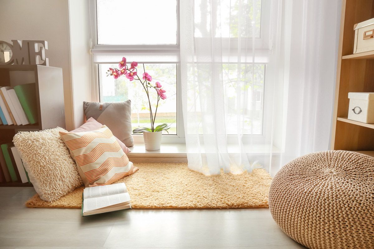 ein Wohnzimmer mit einem Fensterplatz mit Kissen und einem Buch darauf - Gardinen von Koke Raumausstattung - Tobias Liebrand - vor Ort in Senden und Lüdinghausen