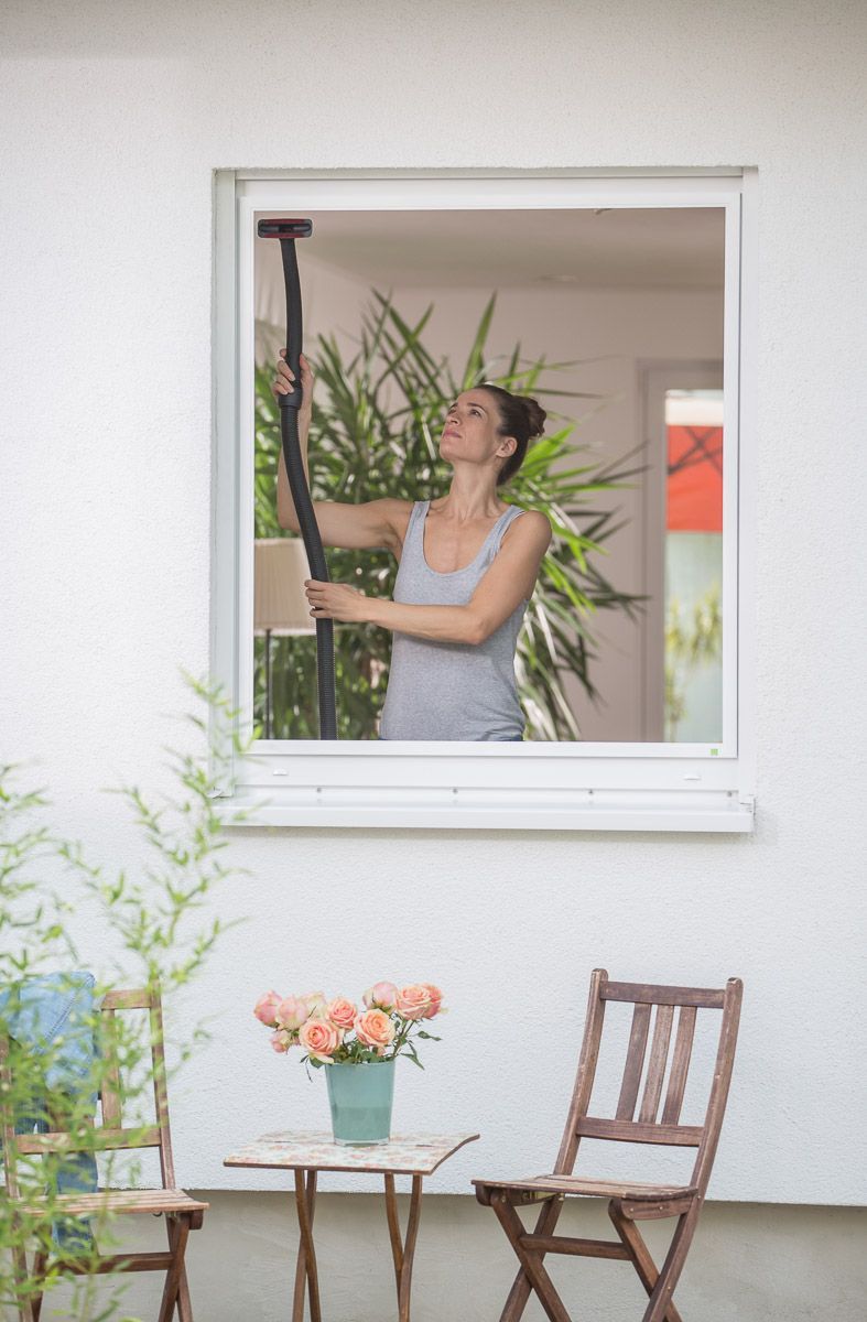 Eine Frau reinigt ein Fenster mit einem Staubsauger - Insektenschutz von Koke Raumausstattung - Tobias Liebrand - vor Ort in Senden und Lüdinghausen