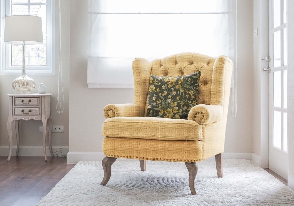 ein gelber Stuhl mit einem grünen Kissen sitzt in einem Wohnzimmer - Polsterei von Koke Raumausstattung - Tobias Liebrand - vor Ort in Senden und Lüdinghausen