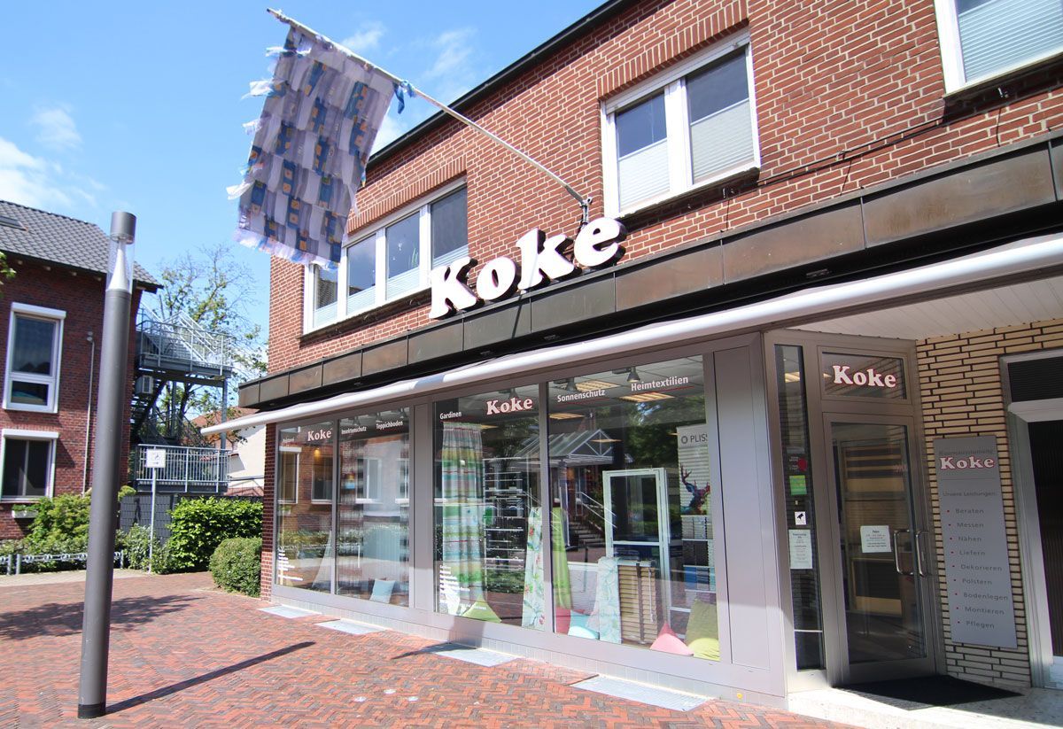 ein braunes Backsteingebäude mit einem großen Fenster und der Aufschrift - Koke Raumausstattung - Tobias Liebrand - vor Ort in Senden und Lüdinghausen